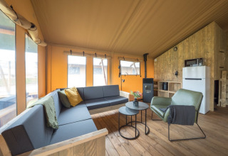 Cozy safari tent interior with wooden flooring, modern seating, large windows, and a kitchen area.