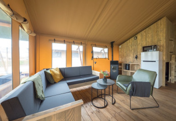 Intérieur confortable d'une tente safari avec plancher en bois, mobilier moderne et grandes fenêtres.