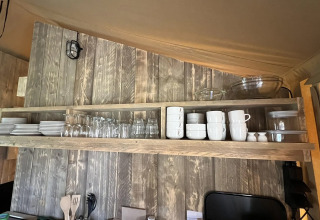 Open houten rek in een safaritent-keuken met netjes gerangschikte borden, glazen en kommen.