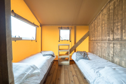 Binnenzicht van een safaritent met twee enkele bedden, houten vloer en warm verlichte wanden.