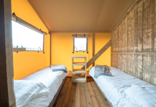 Binnenzicht van een safaritent met twee enkele bedden, houten vloer en warm verlichte wanden.