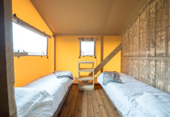 Intérieur d'une tente safari avec deux lits simples, sol en bois et murs éclairés d'une lumière chaude.