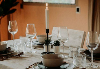 Elegant gedeckter Esstisch in einem Safarizelt mit Kerze, Gläsern, Tellern und kleinen Pflanzen.