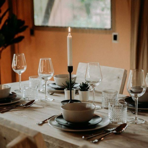 Table joliment dressée dans une tente safari avec bougie allumée, verres, assiettes et petites plantes.