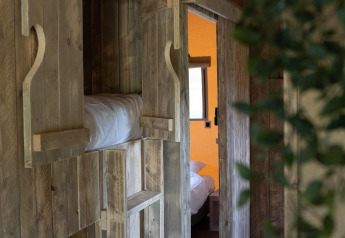 Holzinterieur eines Safarizeltes mit Etagenbett, Leiter, offenem Fenster und Blick in ein Schlafzimmer.