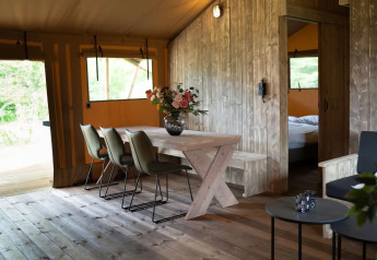 Interior de una lujosa tienda de glamping safari con mesa de comedor y flores en Glampingtent Lina, Países Bajos.