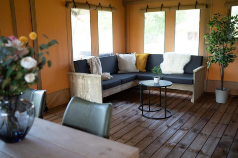 Sfeervolle zithoek in Glampingtent Lina bij Glamping Franse Peer, Nederland, met bank en planten.