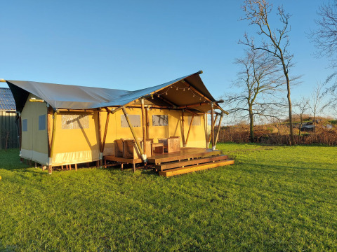 Glampingtent Lina op een groene weide met houten terras en stoelen, in de Belgische natuursetting.