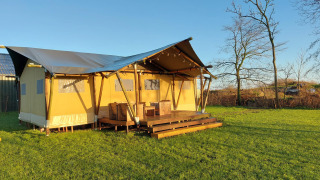 Glampingzelt Lina bei Sonnenlicht auf einer grünen Wiese mit Holzterrasse und Gartenmöbeln.