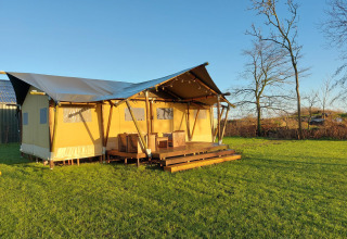 Glampingtent Lina op een groene weide met houten terras en stoelen, in de Belgische natuursetting.