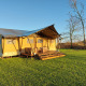 Tienda de glamping Lina en un campo césped con terraza de madera y muebles exteriores al atardecer.