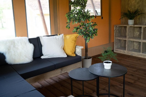 Knusse leefhoek in safaritent Glampingtent Lina met donker zitmeubel, kussens en groene planten.