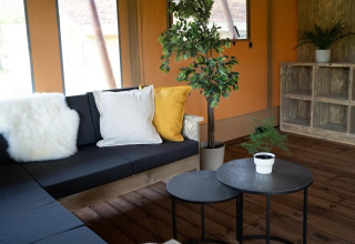 Knusse leefhoek in safaritent Glampingtent Lina met donker zitmeubel, kussens en groene planten.