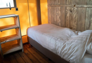 Binnenzicht van Glampingtent Lina bij Glamping Franse Peer in Nederland, met bed en houten rek.