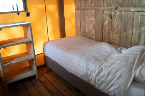 Interieur van Glampingtent Lina bij Glamping Franse Peer in Nederland, met een bed en houten kast.