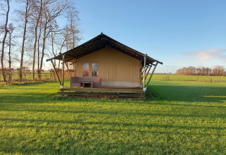 Afbeelding van Glampingtent Joukje, een safaritent op een groen grasveld met bomen en blauwe lucht.