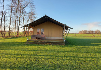 Foto della Glampingtent Joukje, una tenda safari su un prato verde con alberi e cielo azzurro sullo sfondo.