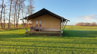 Foto della Glampingtent Joukje, una tenda safari su un prato verde con alberi e cielo azzurro sullo sfondo.