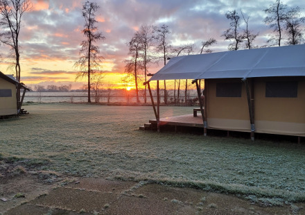 Zonsopgang bij Glamping Franse Peer in Overijssel, Nederland, met tenten en een rijp bedekt grasveld.