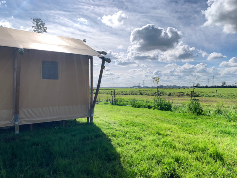 Een glamping-tent in Glamping Franse Peer, Overijssel, Nederland, met zicht op groene velden en wolkenlucht.