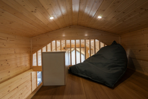 Zona de altillo en una tiny house en Camping Vinkenhof, Países Bajos, con puff y paredes de madera.
