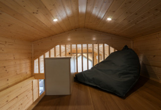 Zona de altillo en una tiny house en Camping Vinkenhof, Países Bajos, con puff y paredes de madera.