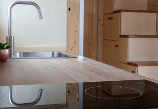Cucina di una tiny house al Camping Vinkenhof, Paesi Bassi, con lavello, fornello e scala con contenitori.