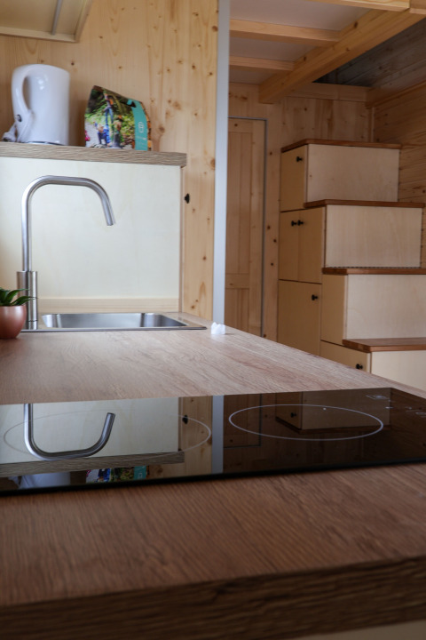 Cucina di una tiny house al Camping Vinkenhof, Paesi Bassi, con lavello, fornello e scala con contenitori.