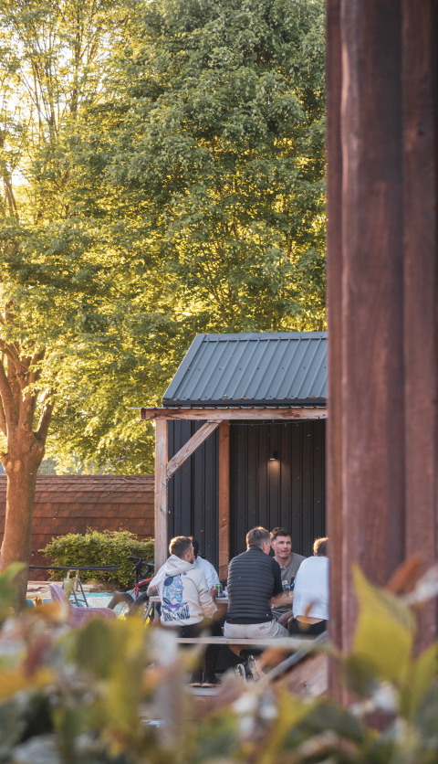 Quattro persone sedute all'aperto a un tavolo da picnic accanto a una tiny house al Camping Vinkenhof, Paesi Bassi.