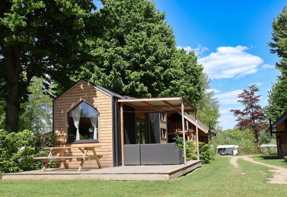 Foto di Tiny House, una piccola casa in legno con terrazza e panchina, immersa nel verde tra gli alberi.