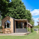 Et billede af Tiny House, et lille træhus med terrasse og bænk, omgivet af grøn natur og træer.