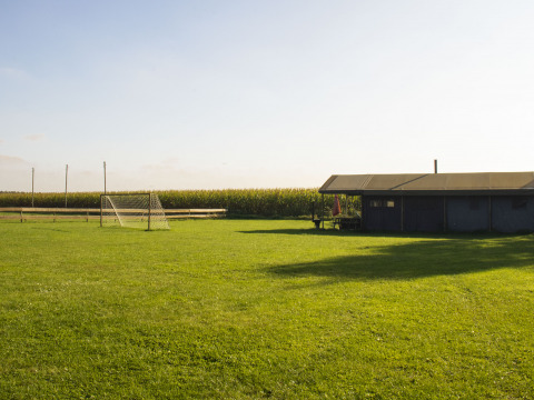 Vakantiepark in Noord-Brabant, Nederland, met voetbaldoel, groene weide en schuur onder de zon.