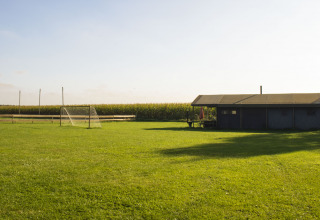 Parco vacanze nel Brabante Settentrionale, Paesi Bassi, con campo da calcio, porta e fienile soleggiato.