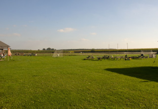 Grøn campingplads med picnicborde, mål og åbent landskab under klar himmel i Nordbrabant, Holland.