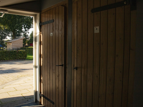 La luz del sol entra por una puerta de madera abierta en Feather Down De Brabantse Hei, parque vacacional en Noord-Brabant.