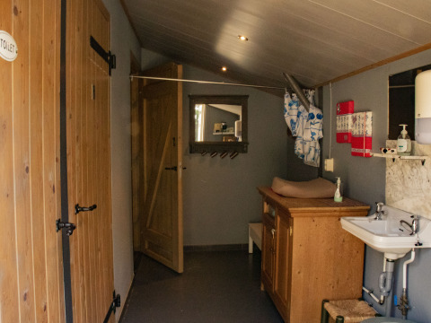 Vista interior de un baño rústico con puertas de madera, lavabo, cambiador y espejo en De Brabantse Hei.