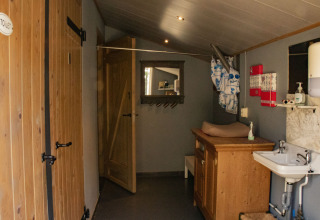 Vista interior de un baño rústico con puertas de madera, lavabo, cambiador y espejo en De Brabantse Hei.