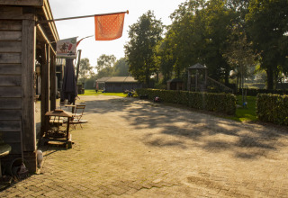 Zonnige binnenplaats bij Feather Down De Brabantse Hei, met terrasstoelen, tafels en groene omgeving.