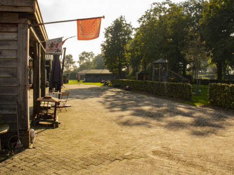 Zonnige binnenplaats bij Feather Down De Brabantse Hei, met terrasstoelen, tafels en groene omgeving.