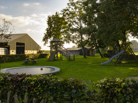 Speeltuin met glijbaan, trampoline en picknicktafels in een groene vakantiepark in Noord-Brabant, Nederland.