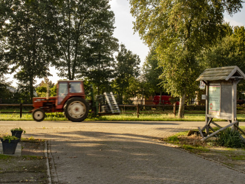 Een rode tractor rijdt langs een informatiebord bij Feather Down De Brabantse Hei vakantiepark in Noord-Brabant, Nederland.