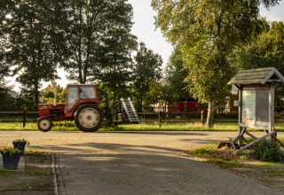 Een rode tractor rijdt langs een informatiebord bij Feather Down De Brabantse Hei vakantiepark in Noord-Brabant, Nederland.