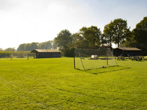 Un campo de fútbol verde con porterías, bancos de madera y cabañas al fondo en De Brabantse Hei, Países Bajos.