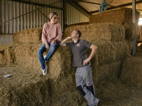 Twee personen kletsen op hooibalen bij Feather Down De Brabantse Hei, Noord-Brabant, Nederland.