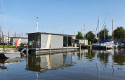 Flydende hus og både ved Marina Heeg feriepark i Friesland, Holland, under en klar blå himmel.