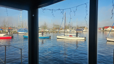 Vue sur des bateaux et la marina du parc de vacances Marina Heeg en Frise, Pays-Bas, à travers une fenêtre.