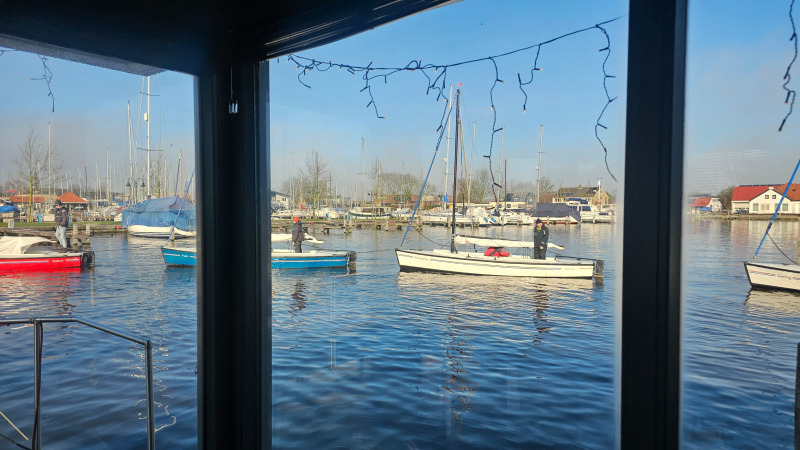 Uitzicht op boten en de jachthaven bij Marina Heeg vakantiepark in Friesland, Nederland, door een raam.