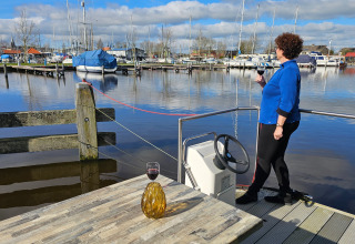 A woman enjoys a glass of wine on a waterside deck overlooking boats at Marina Heeg, Friesland, Netherlands.