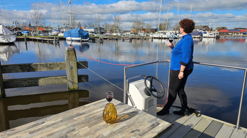 Una mujer disfruta una copa de vino junto al agua con vista a botes en Marina Heeg, Frisia, Países Bajos.