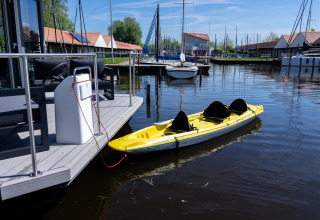 Gele kajak aan een drijvende steiger bij Marina Heeg vakantiepark in Friesland, Nederland, met zeilboten op de achtergrond.